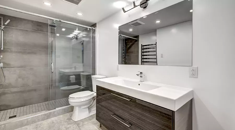 Modern bathroom featuring light wood vanity, brushed brass fixtures, and dark grey stacked tile tub shower